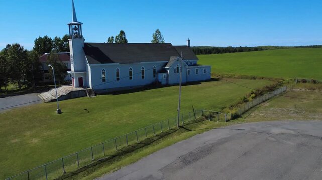 Drone video flying over the roof of a municipal building towards a passageway near the bell tower of the Church of Saint Anthony of Padua, with agricultural fields under a cloudless blue sky. Padoue.