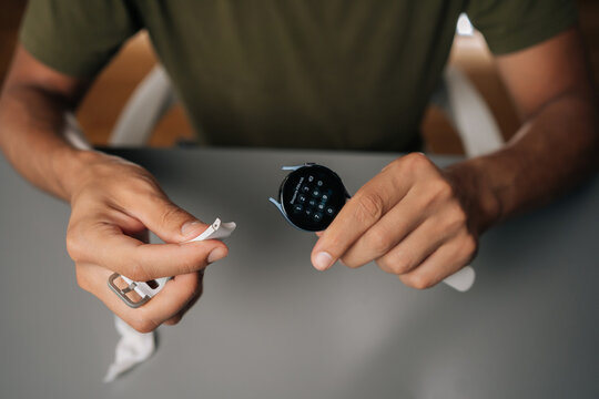 Close-up of male hands assembling white strap onto smart watch, showcasing process of customizing or repairing wearable device sitting at table. Man connecting white smartwatch strap
