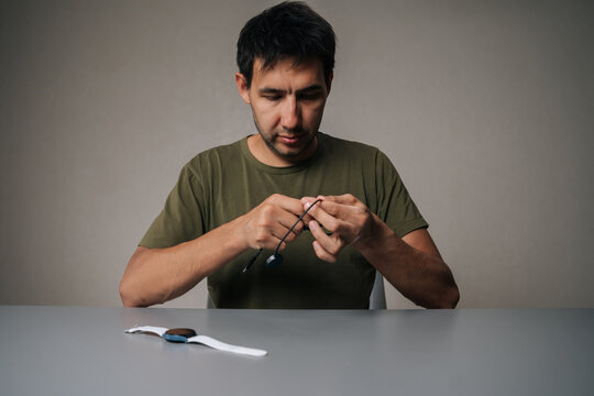 Man holding and untangling black charging cable for smart watch sitting at table with watch on isolated background, emphasizing importance of keeping device powered up. Concept of healthy lifestyle. - Powered by Adobe