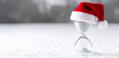 Christmas Countdown Concept &ndash; White Sand Hourglass Topped with Santa Hat on Snowy White Background