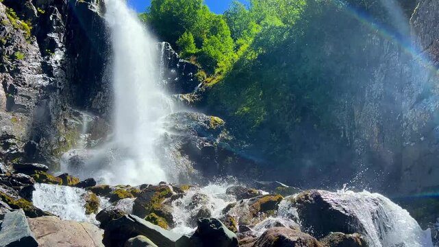 Dombai-Ulgen Gorge, Chuchhur waterfall is framed by malachite greenery of grasses and dense forests. A waterfall flowing down from a glacier. A two-stage stream with white foam, near the Chuchhur pass