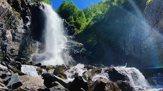 Dombai-Ulgen Gorge, Chuchhur waterfall is framed by malachite greenery of grasses and dense forests. A waterfall flowing down from a glacier. A two-stage stream with white foam, near the Chuchhur pass