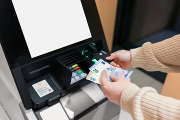 Hands holding Euro banknotes near ATM with blank white screen. Person withdrawing money at bank...