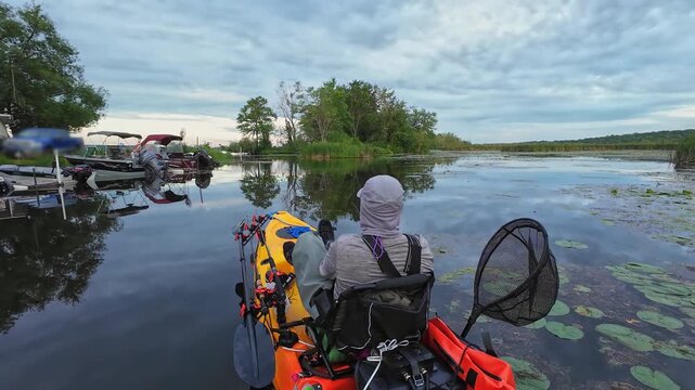 Kayak fishing game, angler at weedy lake pond, fishing pdl kayak during tournament. Sport and bass fishing activity in the morning on pedaling fishing kayak. Water hobby and active lifestyle.