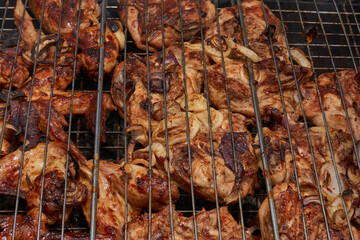 Juicy pieces of chicken are grilled in a metal grill over hot coals. The ruddy crust and smoky...