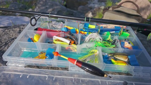 Family leisure water sports fishing. Fishing spinning and casting rods with fishing tackles on rocks near lake shore background, close up. Fishing rods lines, bobber and plastic jigs with worm lures.