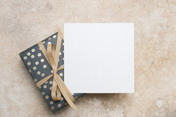 Blank square greeting card mockup on trendy beige background with beautifully wrapped gift, featuring a delicate ribbon, ideal for personalized messages and creative designs