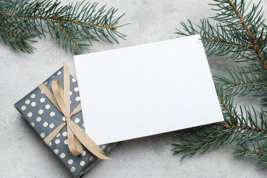 Blan Christmas greeting oor invitation card mockup with copy space, surrounded by evergreen branches and a beautifully wrapped gift box, perfect for seasonal design projects and holiday wishes