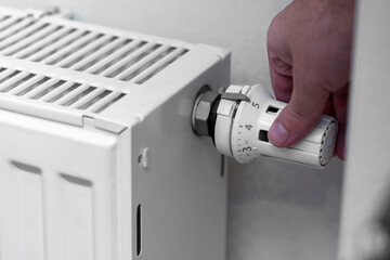 A person adjusts a radiator thermostat to control the heating in a room. The scene highlights effort in maintaining warmth at home during cold seasons.