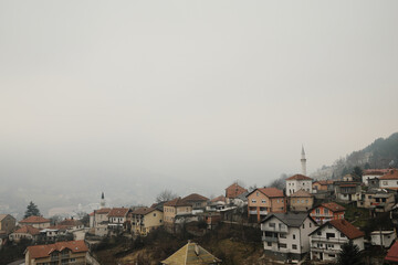 Fototapeta premium Foggy panoramic view of Travnik city in Bosnia and Herzegovina with traditional houses and mosque minaret seen from Travnik Fortress.