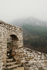 Old stone arch passage inside Travnik Fortress in Bosnia and Herzegovina with misty mountain forest in the background.