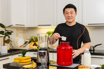 Asian young adult man pours whey protein into blender with banana and cottage cheese preparing shake. Protein smoothie supports muscle gain weight control fitness energy and home kitchen healthy diet.