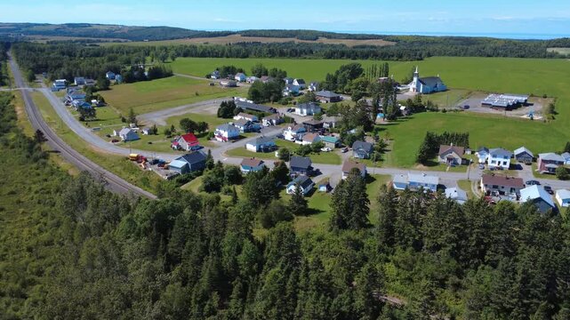 Panoramic aerial view of a small rural village with a red truck driving by. Tiny town of houses between the railway and its church against a backdrop of farmland. Padoue, Quebec, Canada, 2025.