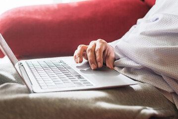 Person using a laptop on a sofa at home, close up of hand on touchpad