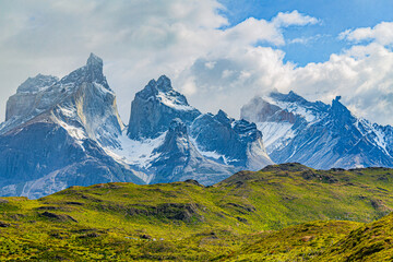 Rugged Cuernos del Paine peaks tower over the green hills below as clouds drift across the sky in Torres del Paine National Park, Chile. © ZL Visuals