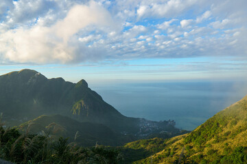 Fototapeta premium A wide view of a green mountain valley opening toward the sea under a blue sky, capturing peaceful nature, landscape depth, and outdoor travel scenery.