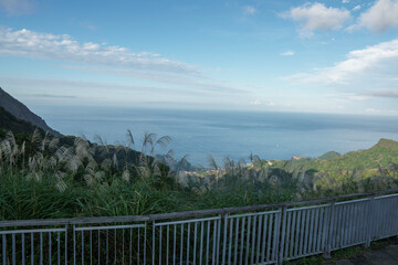 Fototapeta premium A wide view of a green mountain valley opening toward the sea under a blue sky, capturing peaceful nature, landscape depth, and outdoor travel scenery.