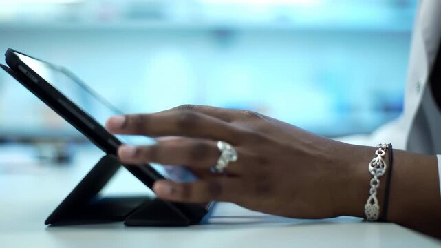 Close up on hands using a tablet on a white desk in a bright room. Features modern technology and dark skin with cool jewelry. Focus on user interaction.