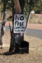 No Free Camping - Trucks Only handmade sign attached to a tree with a dark wicker chair