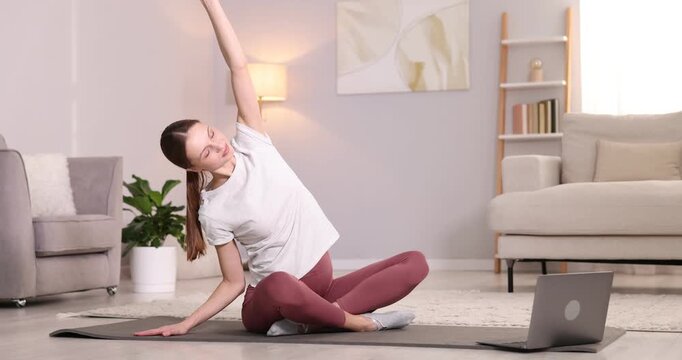Pregnant woman having online yoga class via laptop at home