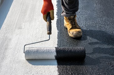 Close-up of a person applying black coating to a white surface with a roller