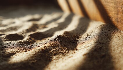 Close-up of dry, textured sand with sunlight casting shadows from wooden structure
