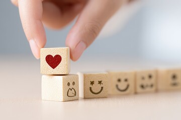 Hand placing a wooden block with a heart on top of a stack of blocks with various facial expressions