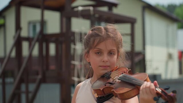 White Girl Practicing Violin Near Playground, Suburban Backdrop With Climbing Frame And Houses, Casual Outdoor Lesson, Poised Bowing, Youthful Determination And Summertime Atmosphere