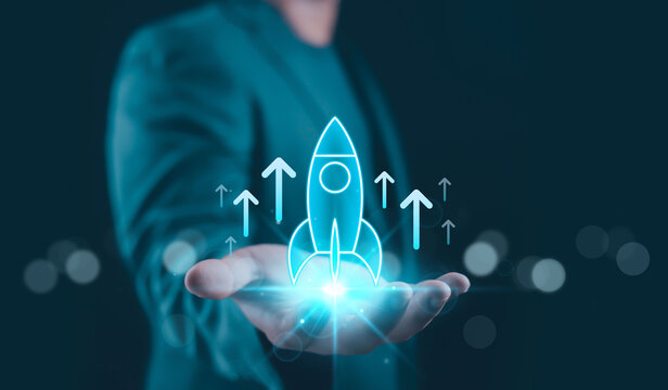 Glowing rocket icon above businessman hand with upward arrows, representing startup growth, business acceleration, digital innovation, performance improvement and future-oriented technology success.