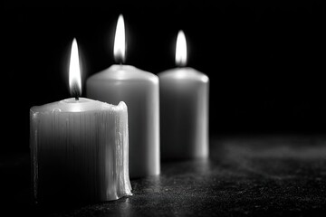 Three lit candles on dark surface in low light, creating a somber mood