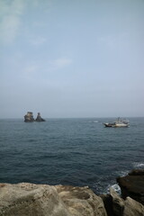 Obraz premium Fishing Boat Sailing Near Coastal Rock Formations