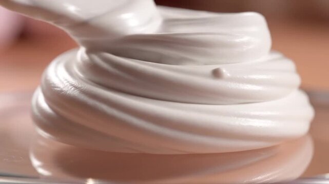 Close-Up Shot of White Cream Swirl on a Clear Surface with a Soft Pink and Beige Gradient Background Perfect for Confectionery and Dessert-Related