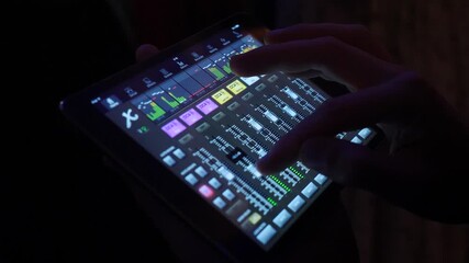Professional sound engineer uses dj console tablet near stage, controlling sound of music band. High-tech mixing tablet illuminated with light. Volume indicators running on screen. Professional sound