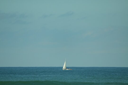 
A white sailboat navigates the blue horizon under a vast, clear sky. - Um veleiro branco navega pelo horizonte azul sob um vasto c&eacute;u limpo