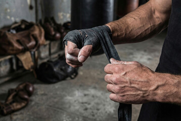 Fighter wrapping hands with black boxing tape before training in old grunge gym