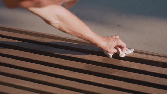Individual Wiping Wooden Seat, Caucasian Individual Meticulously Cleaning Park Bench In Sunlight, Man With Cloth Tending To Wooden Bench Under Sunlight Showing Careful Attention And Tension