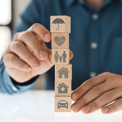 Hands carefully stacking wooden blocks with diverse icons, symbolizing comprehensive insurance coverage, essential life planning, and future security for individuals and families