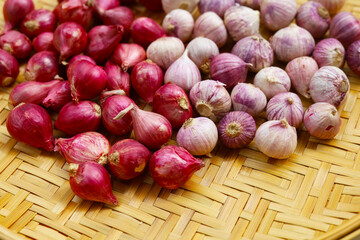 Fresh red shallots with single clove garlic bulbs on bamboo tray