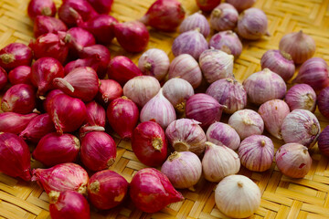 Fresh red shallots with single clove garlic bulbs on bamboo tray