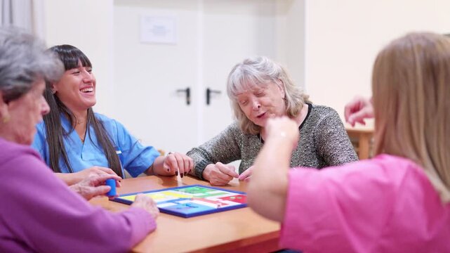 Senior women playing a parcheesi board game with caregivers