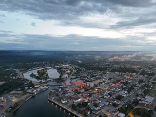 Naklejka premium Aerial view of Matane city at dusk with river, fog, low clouds and city lights along St Lawrence River, Quebec, Canada. g.