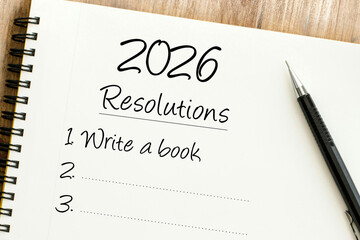 Handwritten 2026 Resolutions list in a spiral notebook with Write a book as the first goal and a pen on side.