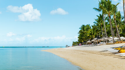Escape to pristine sands, turquoise waters, and swaying palms! This idyllic beachfront scene captures relaxation and leisure. Sunlit cabanas, kayaks, and a vibrant sky evoke carefree indulgence.