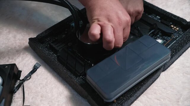Male hands secure the round water block of a liquid cooling system onto the processor, tightening screws on the motherboard mount