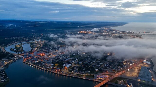 Aerial view of Matane city at dusk with river, fog, low clouds and city lights along St Lawrence River, Quebec, Canada. g.