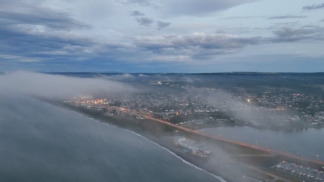 Aerial view of Matane city at dusk with river, fog, low clouds and city lights along St Lawrence River, Quebec, Canada. g.