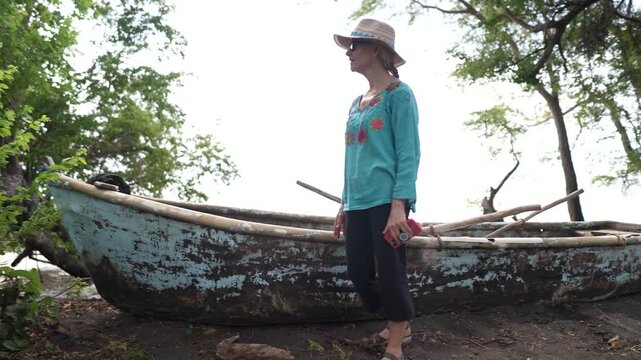 A mature woman admires a wooden rowboat on Ometepe Island in Nicaragua surrounded by jungle and nature near Costa Rica.
