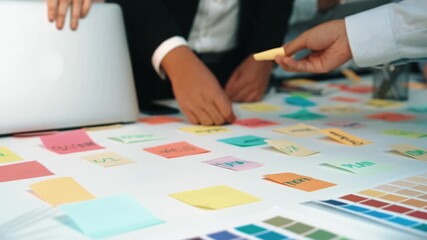 A collaborative workspace captures focused hands selecting colorful sticky notes while discussing ideas over a laptop, emphasizing teamwork and creativity in a professional setting. SACTR