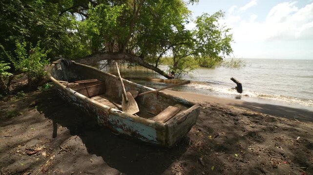 Wooden rowboat rests on the shore of Ometepe Island in Nicaragua with jungle nearby and water in the background