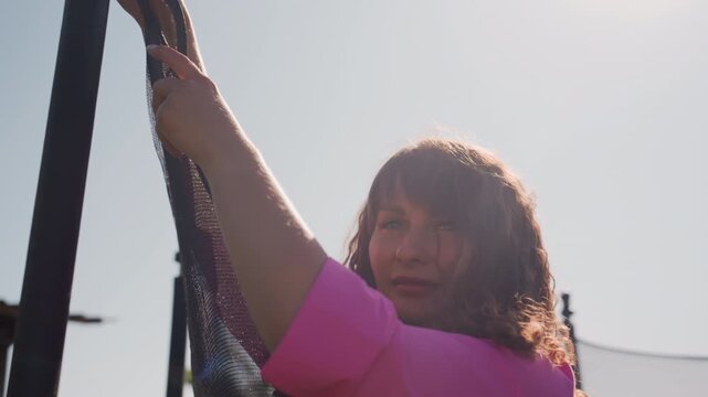 Centering On Trampoline Safety Procedures, Close View Of Hands Securing Trampoline Net Amidst Sunlight, Individual Meticulously Fastening Safety Net To Trampoline Pole During Sunny Outdoor Setting